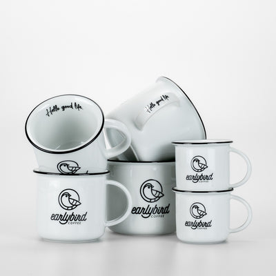 earlybird Kaffeetassen Set bestehend aus zwei Espressotassen, zwei Kaffeetassen und zwei Kaffeebechern aus weißem Keramik mit schwarzem Tassenrand und earlybird coffee Logo jeweils zwei Tassen aufeinandergestapelt