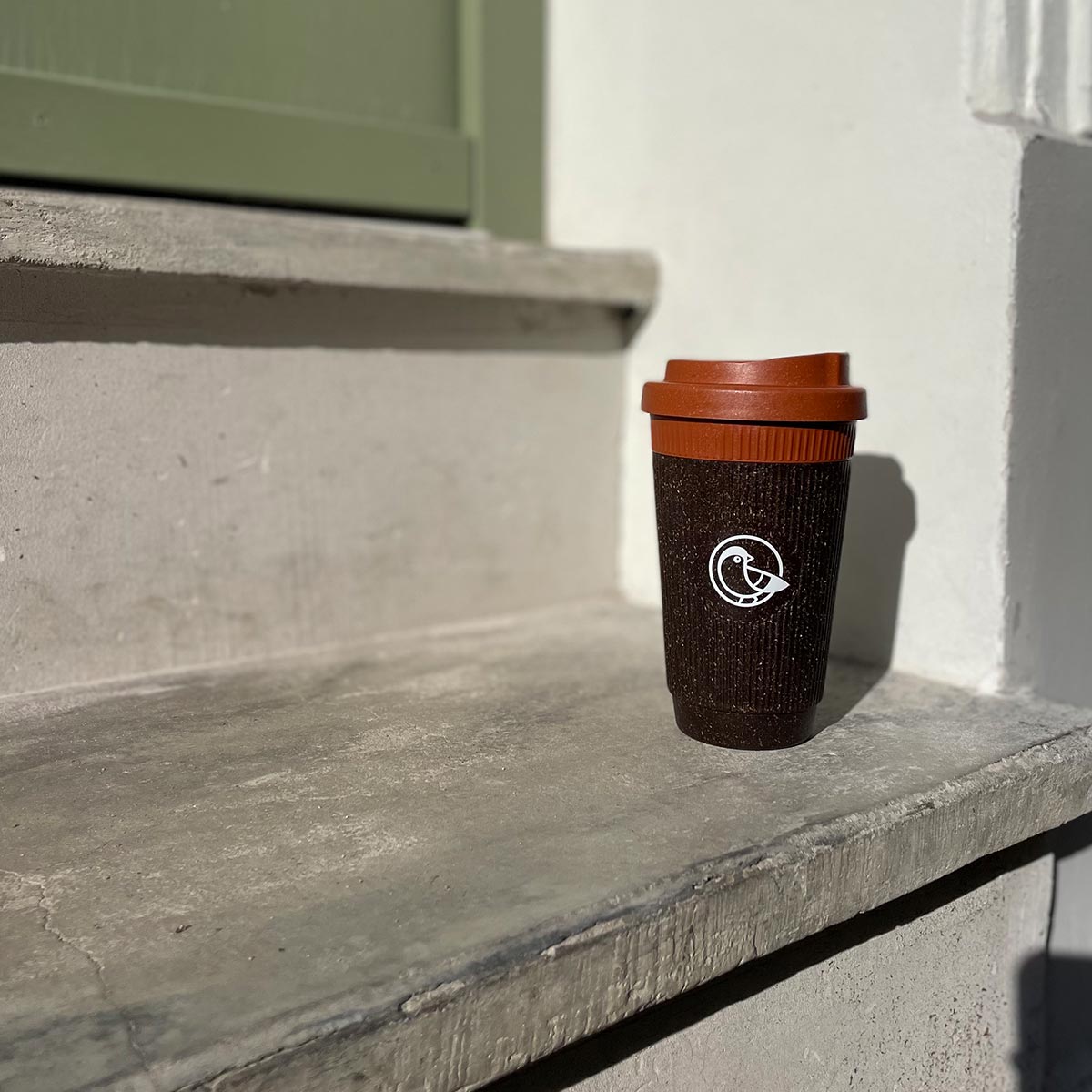 earlybird Coffee to Go Becher aus recyceltem Kaffeesatz steht auf einer Treppe in der Sonne