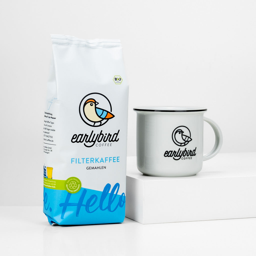 earlybird 250g Packung Filterkaffee gemahlen lehnt an der earlybird Kaffeetasse aus Porzellan mit earlybird coffee-Logo