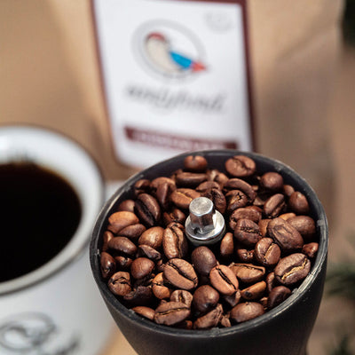 earlybird Kaffee mit Schokoladennote Bohnen in Handmühle neben Tasse mit schwarzem Kaffee