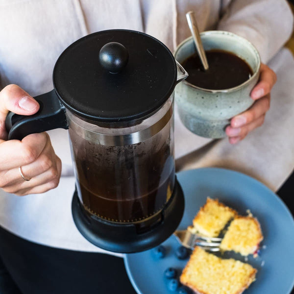 In der French Press zubereiteter earlybird Cafe Crema wird eingeschenkt und mit einem Stück Kuchen genossen.